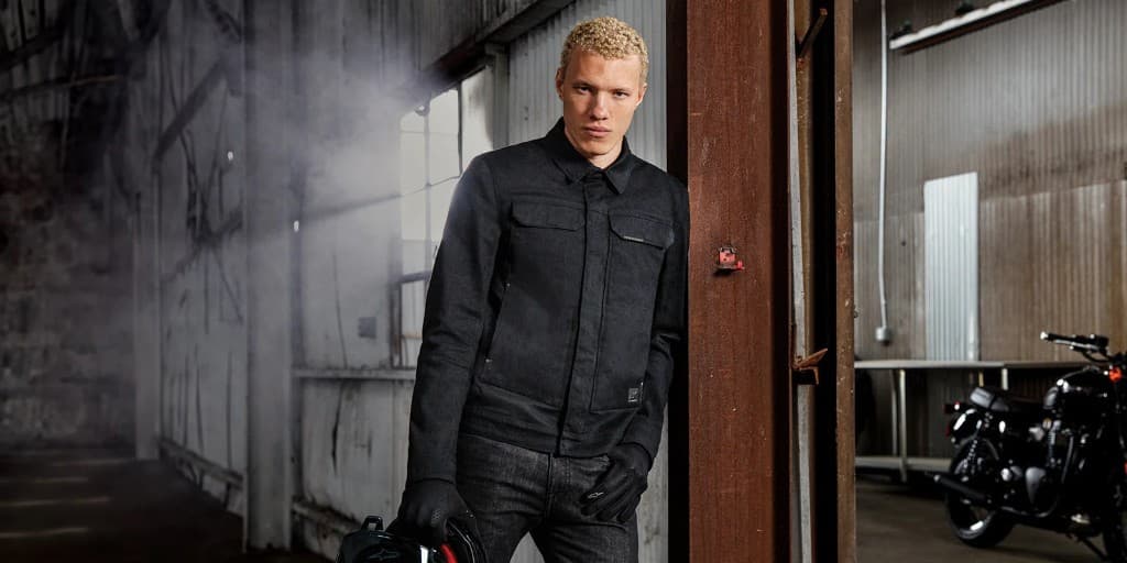 Rider wearing an Alpinestars casual denim-style motorcycle jacket in an industrial warehouse setting