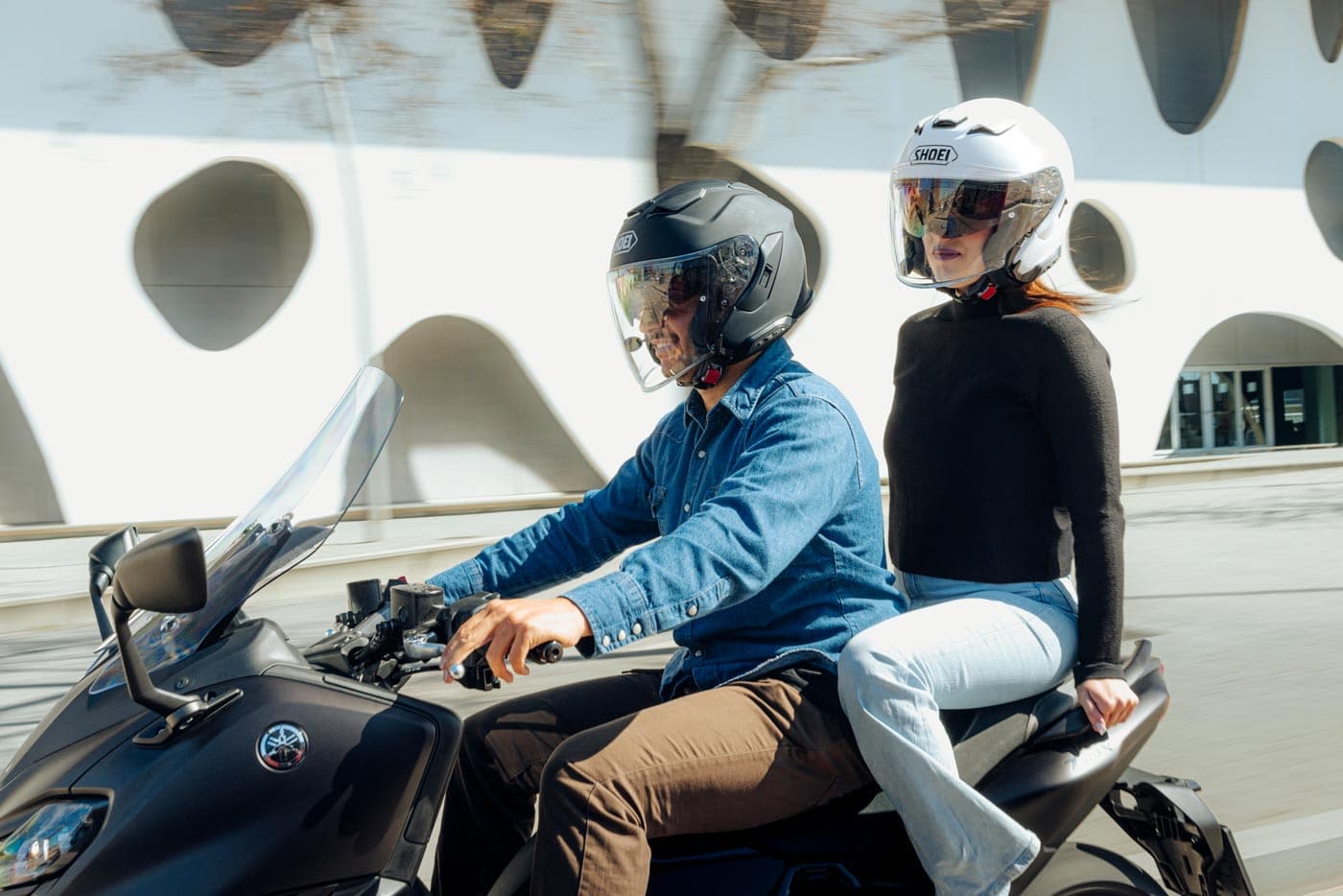Woman and man riding a Yamaha scooter wearing stylish white and black Shoei open-face motorcycle helmets