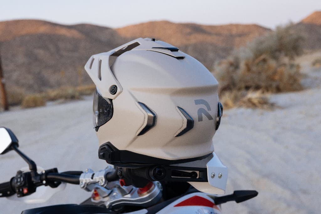 Matte grey lightweight adventure motorcycle helmet resting on handlebars with a desert landscape in the background