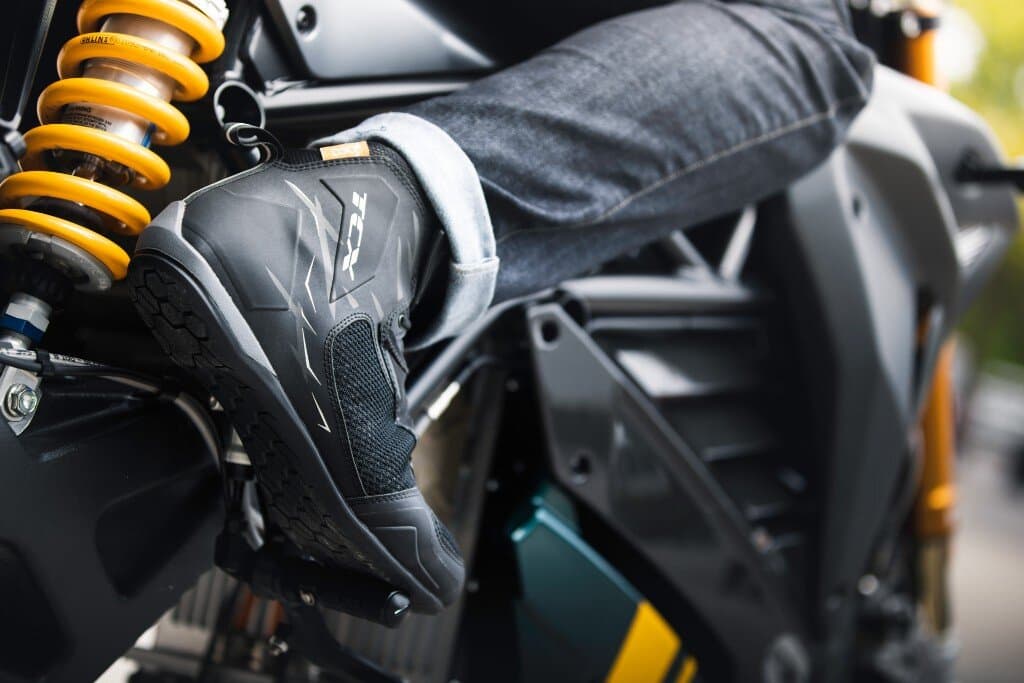 TCX motorcycle riding shoe worn by a rider seated on a motorcycle with Ohlins suspension visible