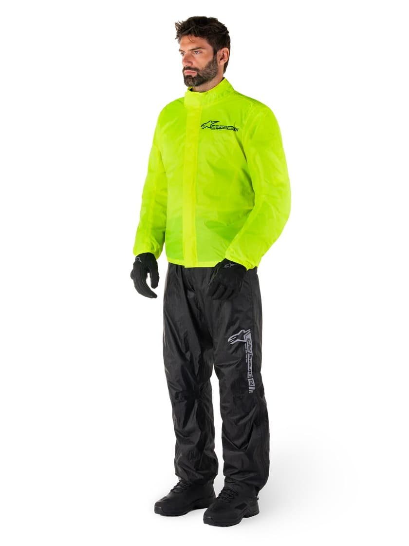 Man wearing a two-piece Alpinestars motorcycle rain suit with high-visibility neon yellow jacket and black waterproof pants