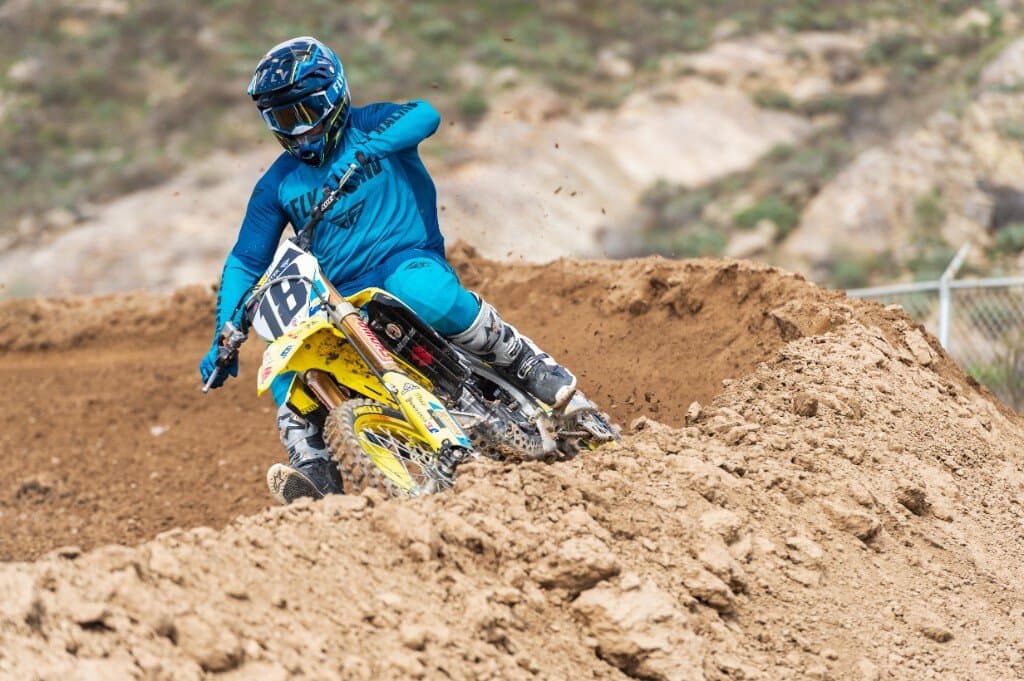 Motocross rider in white Alpinestars boots leaning into a turn on a dirt track