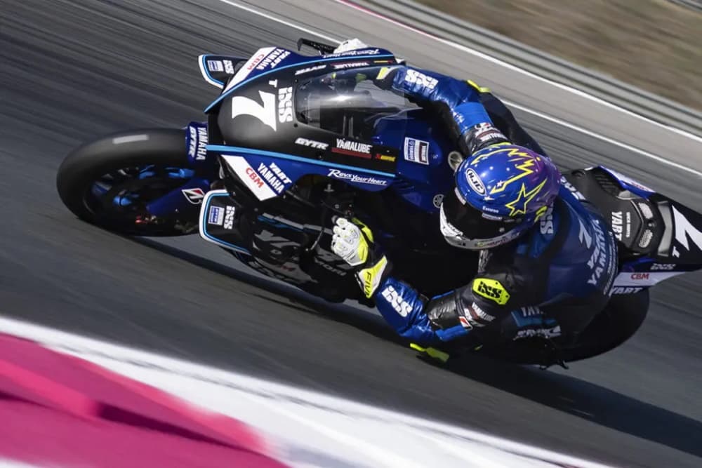 Professional motorcycle racer leaning into a corner on a Yamaha track bike wearing white FIVE racing gloves and a colourful HJC helmet