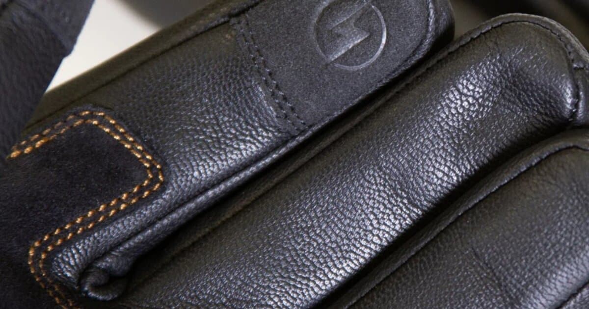 Close-up of black leather winter motorcycle gloves showing padded knuckle protection and touchscreen-compatible fingertips